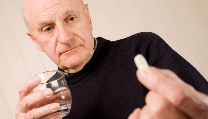 Mature older man holding tablet or pill with water